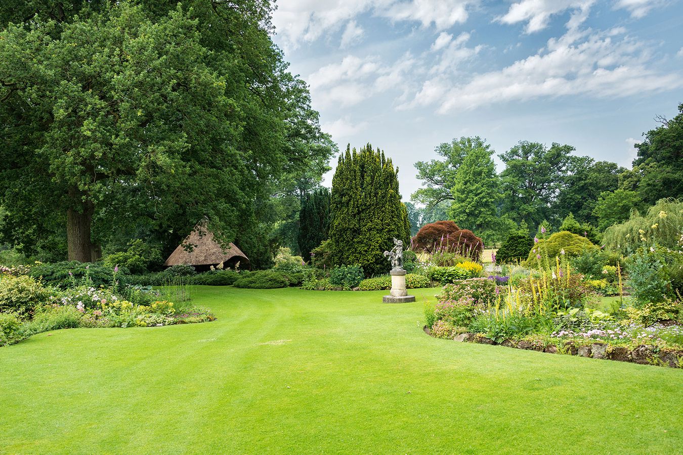 Gepflegter Garten mit einer zur Zierde aufgestellten Statue auf dem Rasen